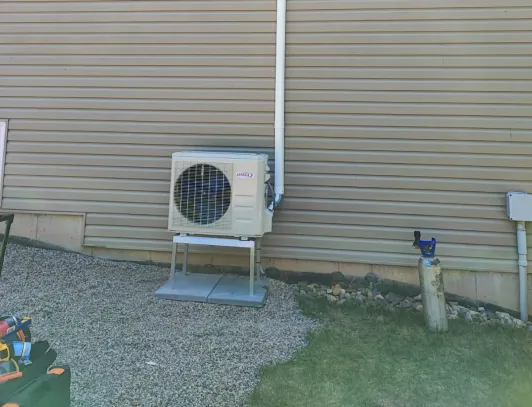 Heat pump condenser installed on grass beside a home with cream vinyl siding