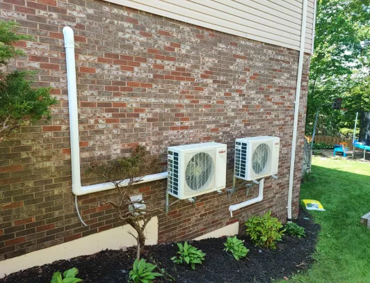 Two heat pump condensers installed against the brick wall of a home with tidy line runs