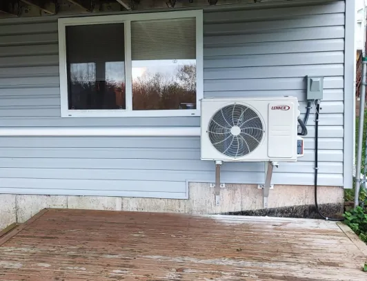 Heat pump condenser on a wall-mounted bracket beside a window on blue siding
